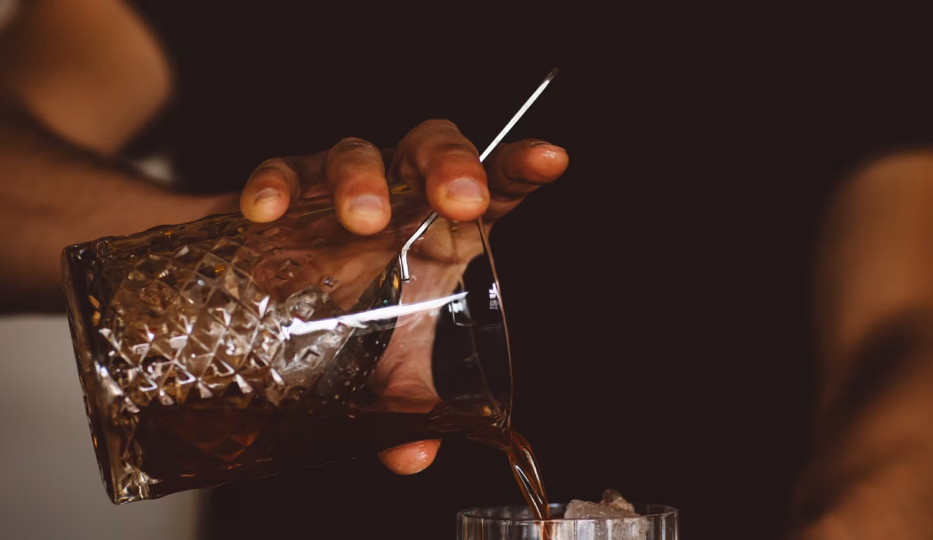 Hand pouring a drink into a cut-glass tumbler at the bar