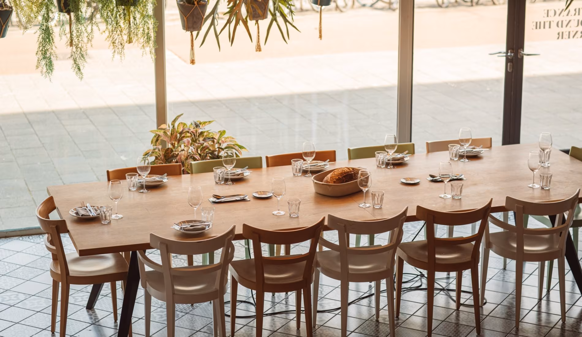 Long wooden table set for a group beside the floor-to-ceiling windows