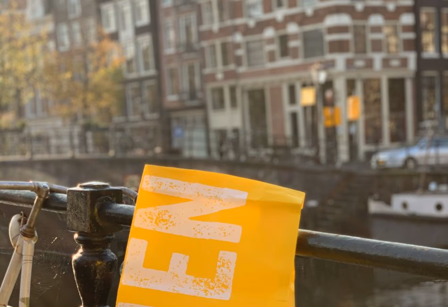 Yellow NENI flag on a bridge railing above an Amsterdam canal
