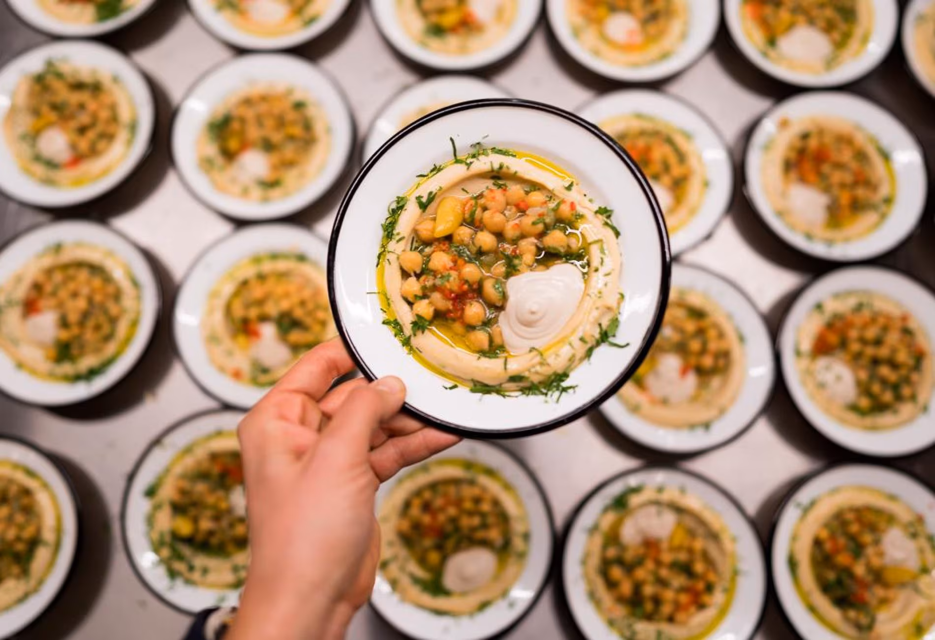 Overhead view of many bowls of hummus topped with chickpeas and herbs