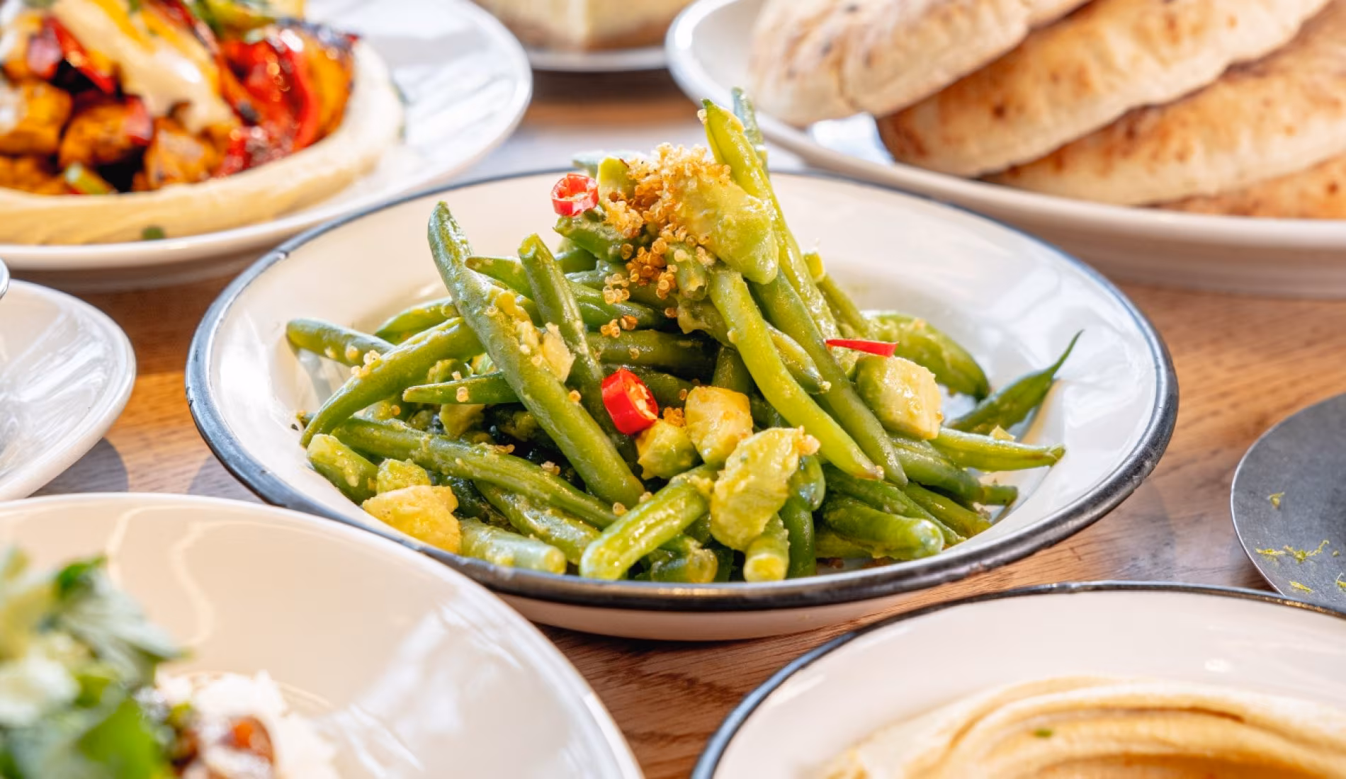 Plate of green beans with mezze, bread and dips on a set table