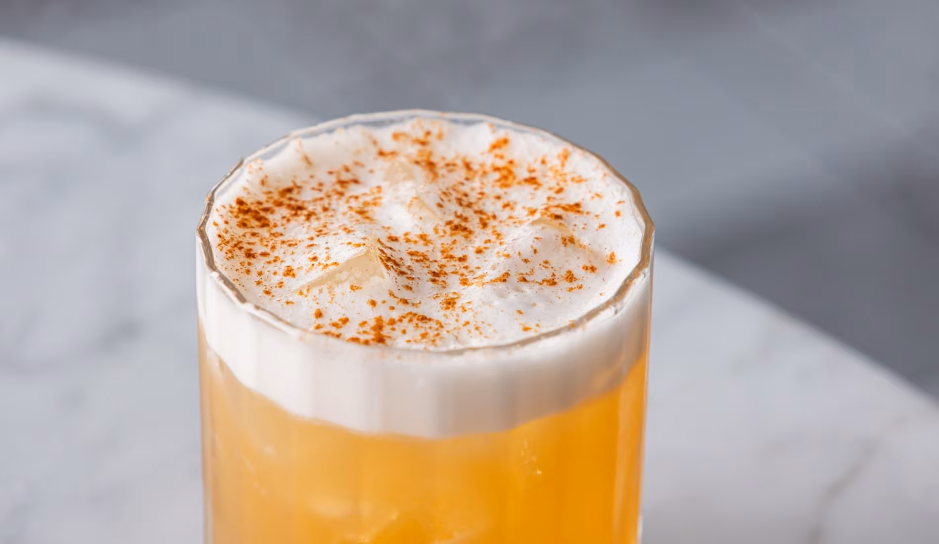 Foamy citrus cocktail dusted with spice, in a glass on a marble counter