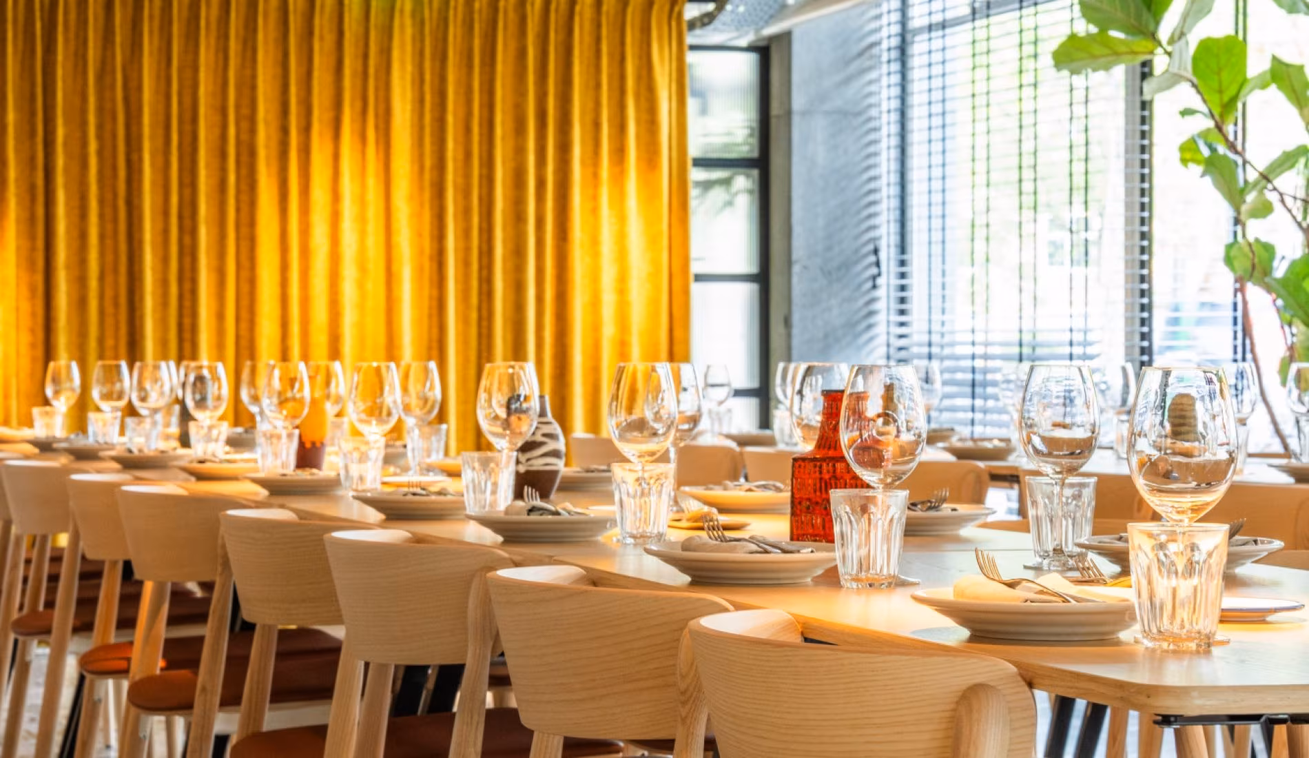 Long table set with glassware in front of yellow curtains