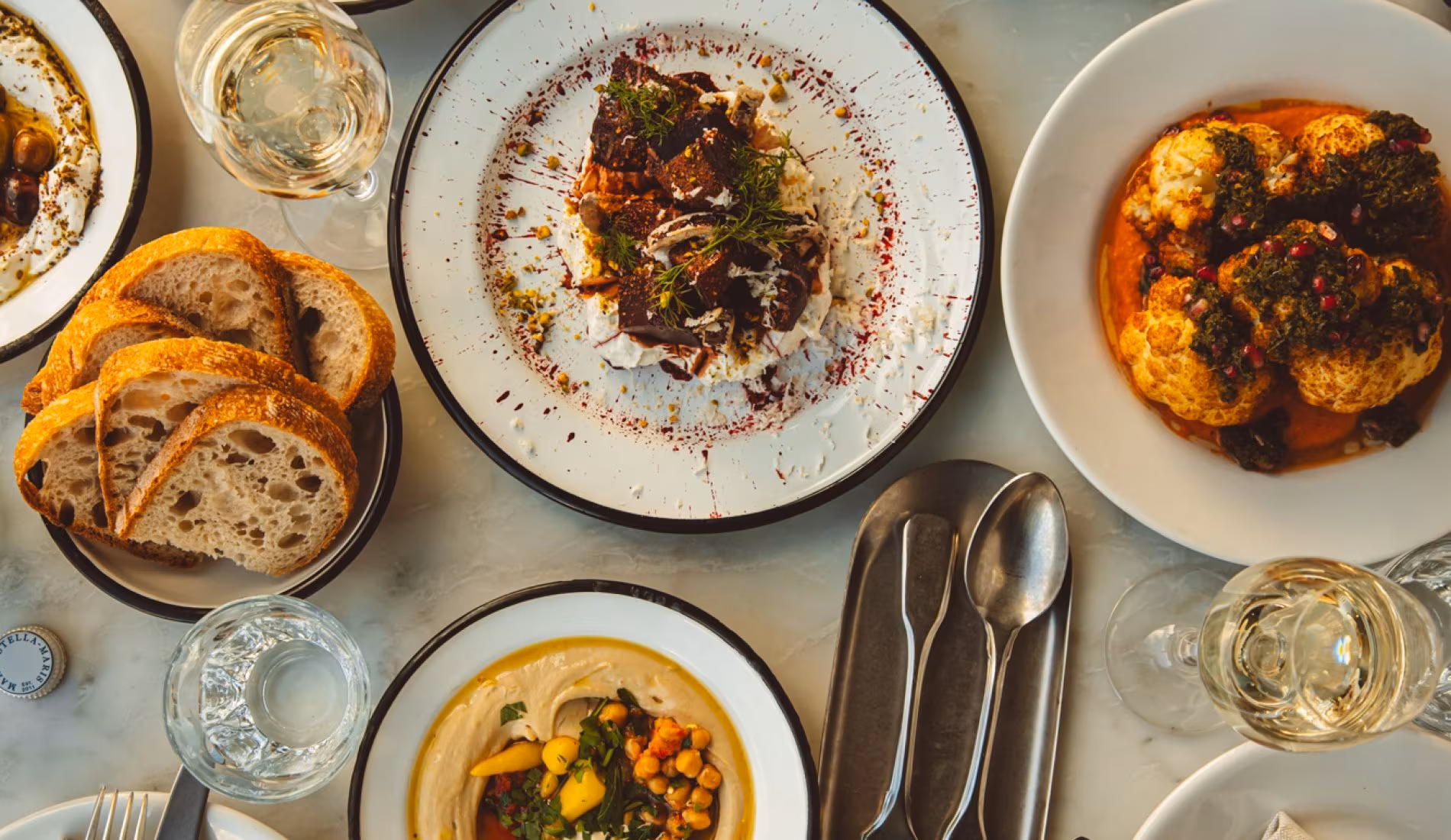 Table set with bread, salads, grilled dishes and wine glasses