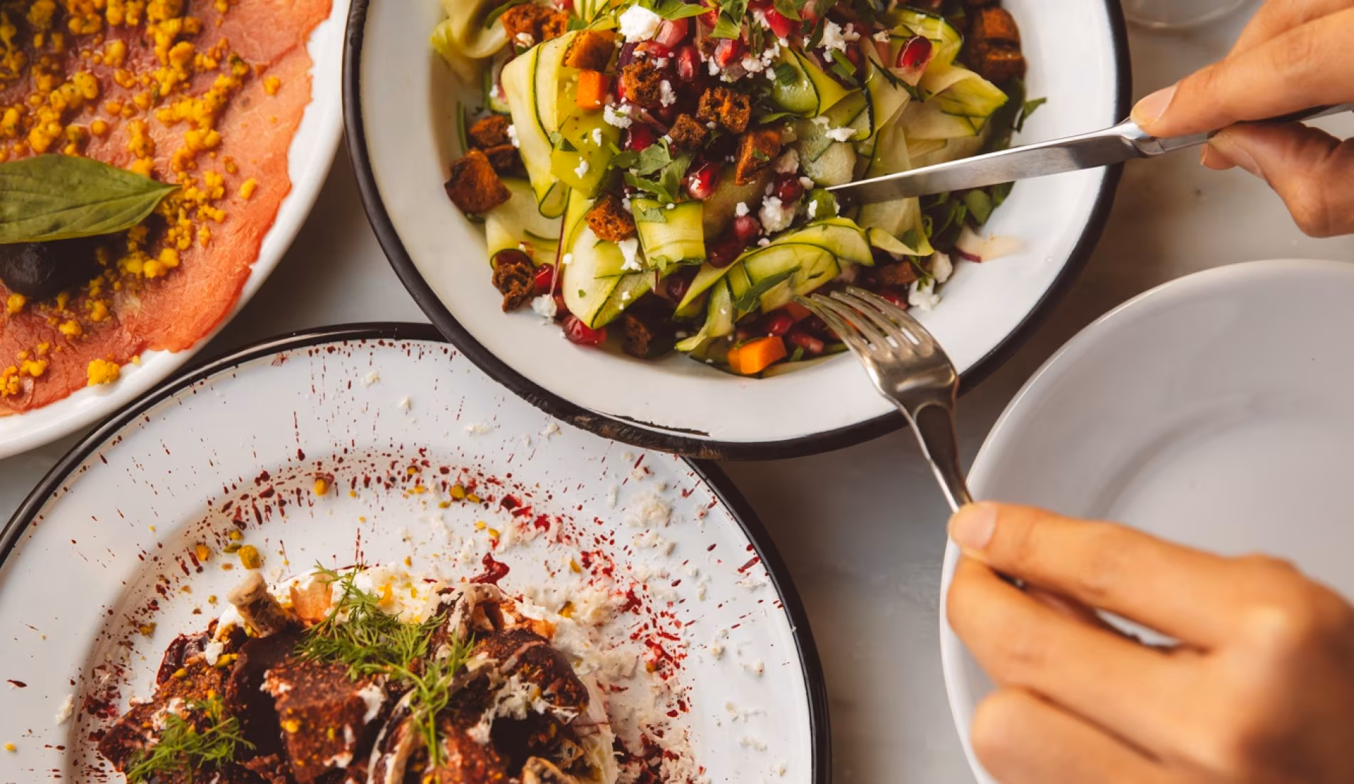 Hand eating a plate of grilled vegetables with dip and pomegranate