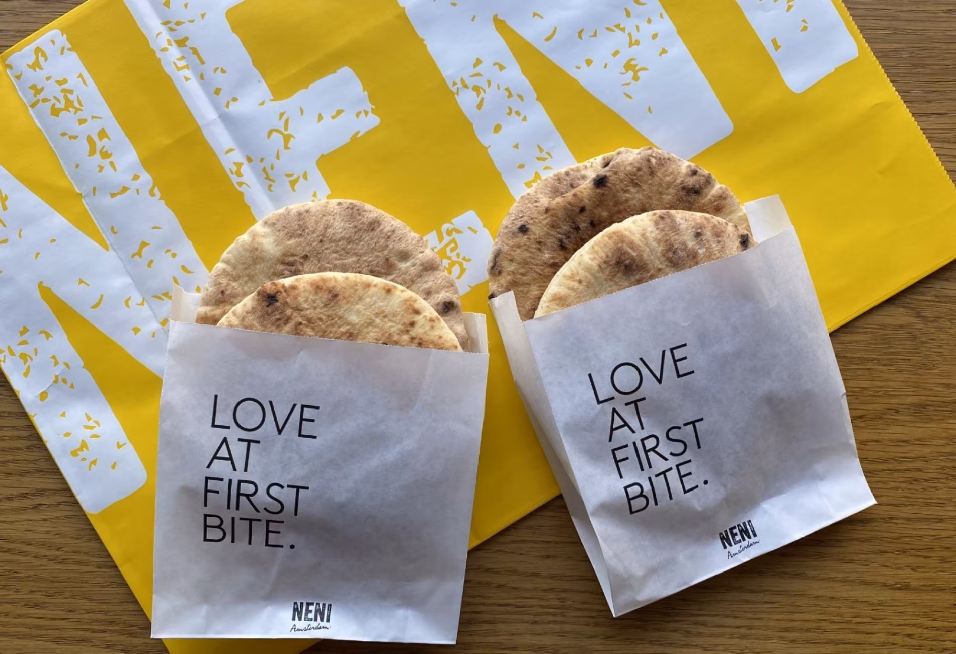 Two Love At First Bite paper bags with pita on yellow NENI paper