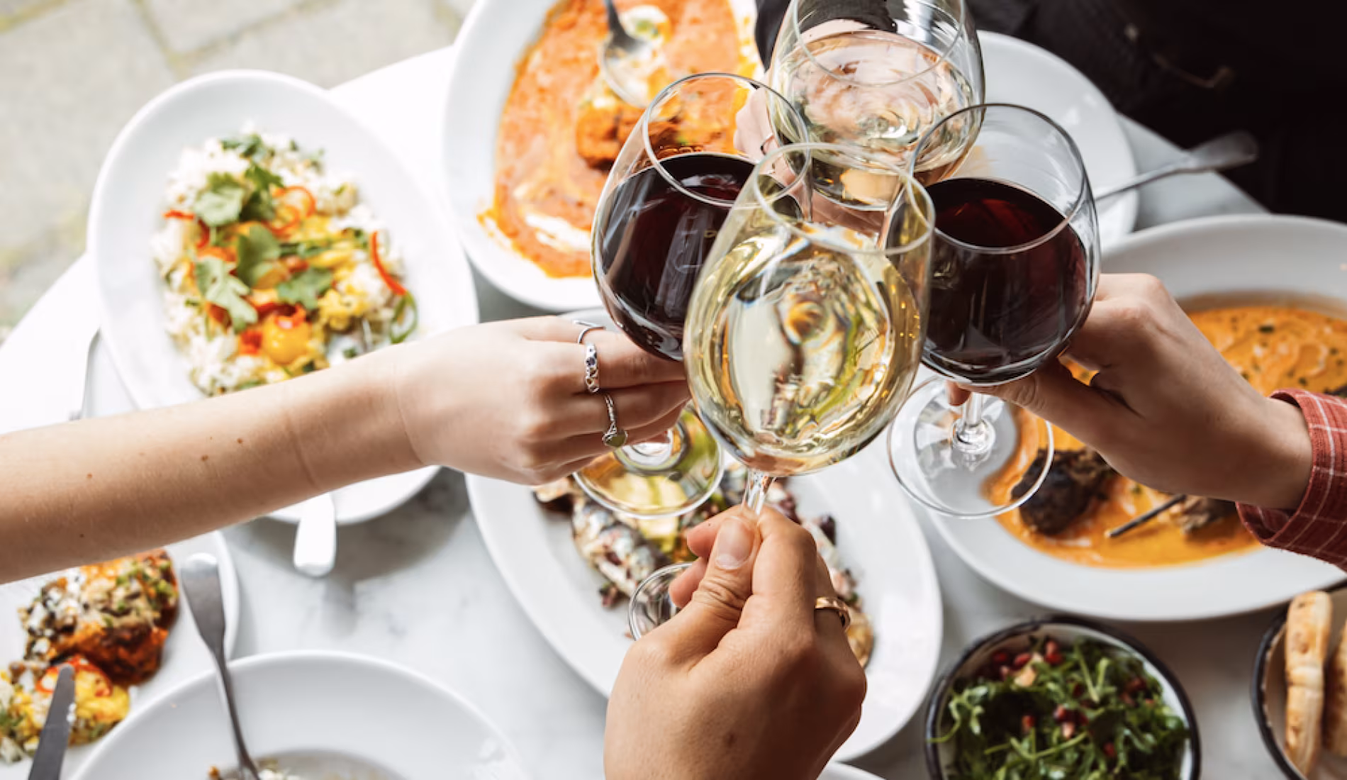 Two guests toasting with wine over a table of lunch dishes