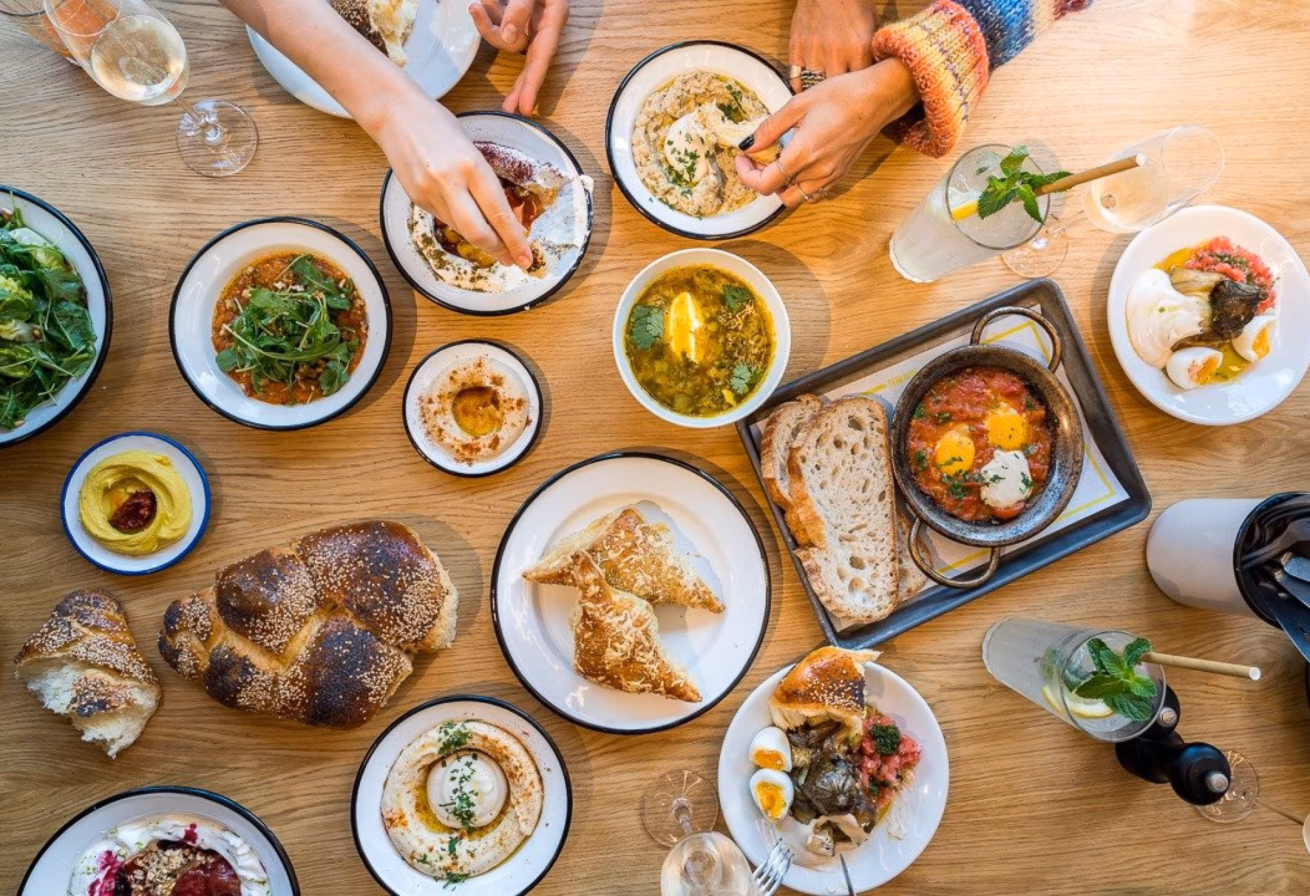 Hands reaching over a wooden table full of mezze, pastries and dips