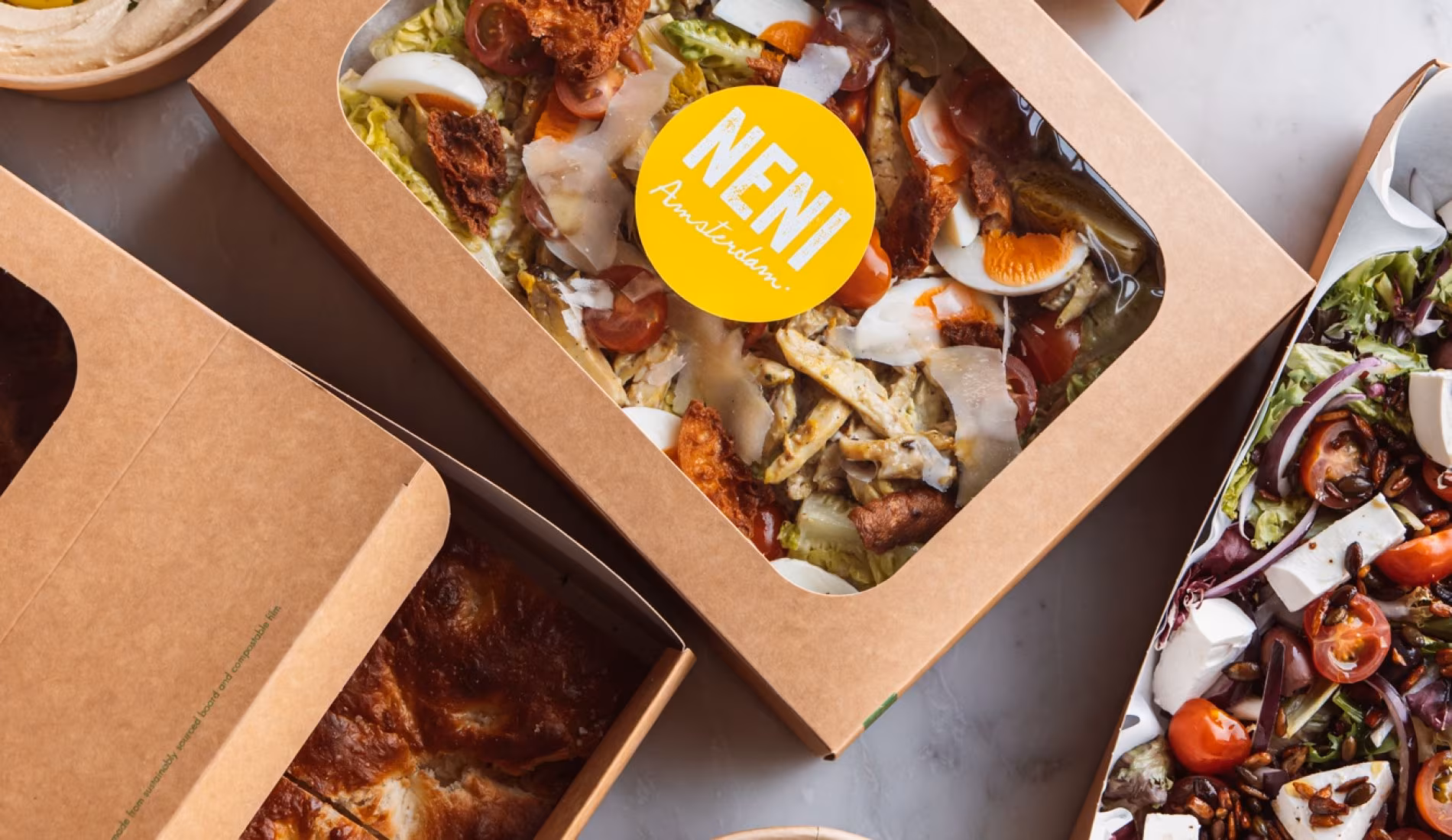 Takeaway boxes with a yellow NENI sticker, filled with salads and mezze