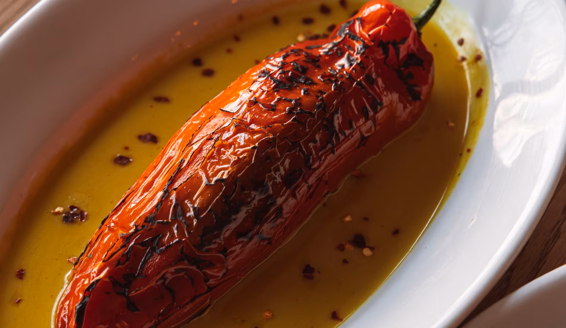 Whole roasted red pepper in olive oil on an oval dish