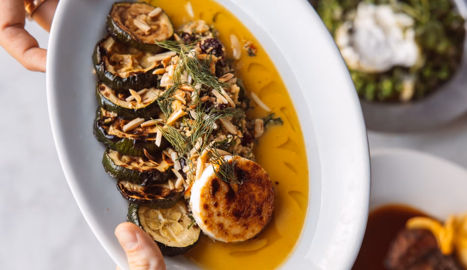 Plate of grilled aubergine with tahini and herbs being served
