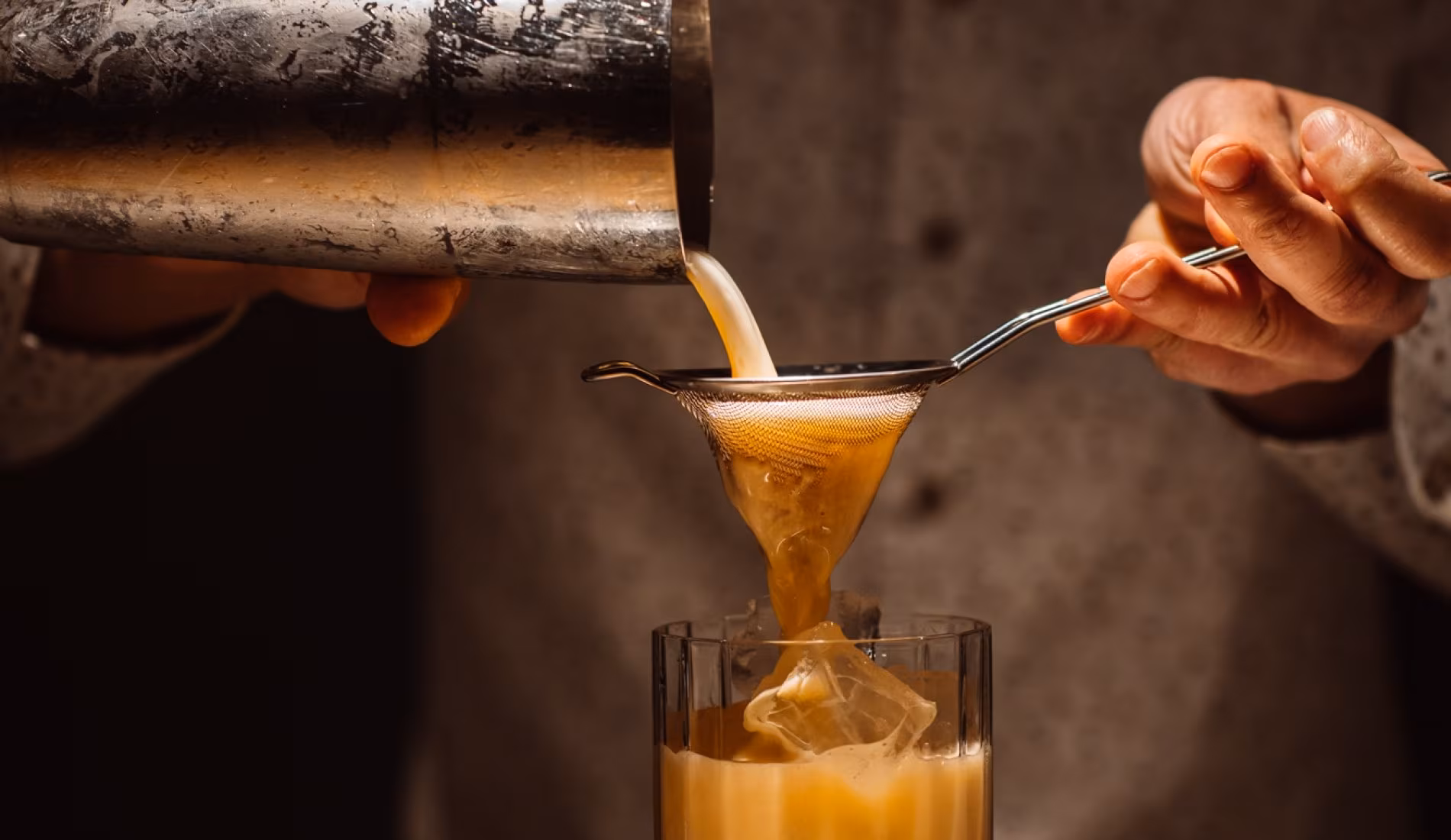 A cocktail being poured and spooned into a glass behind the bar