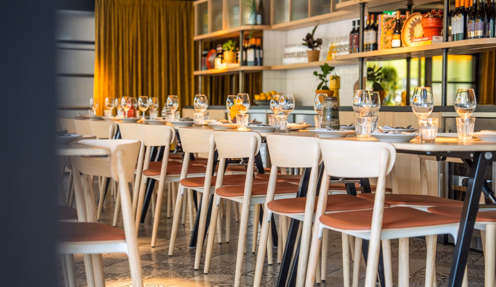 Dining area at NENI Amsterdam with wine shelves and pastel-coloured chairs
